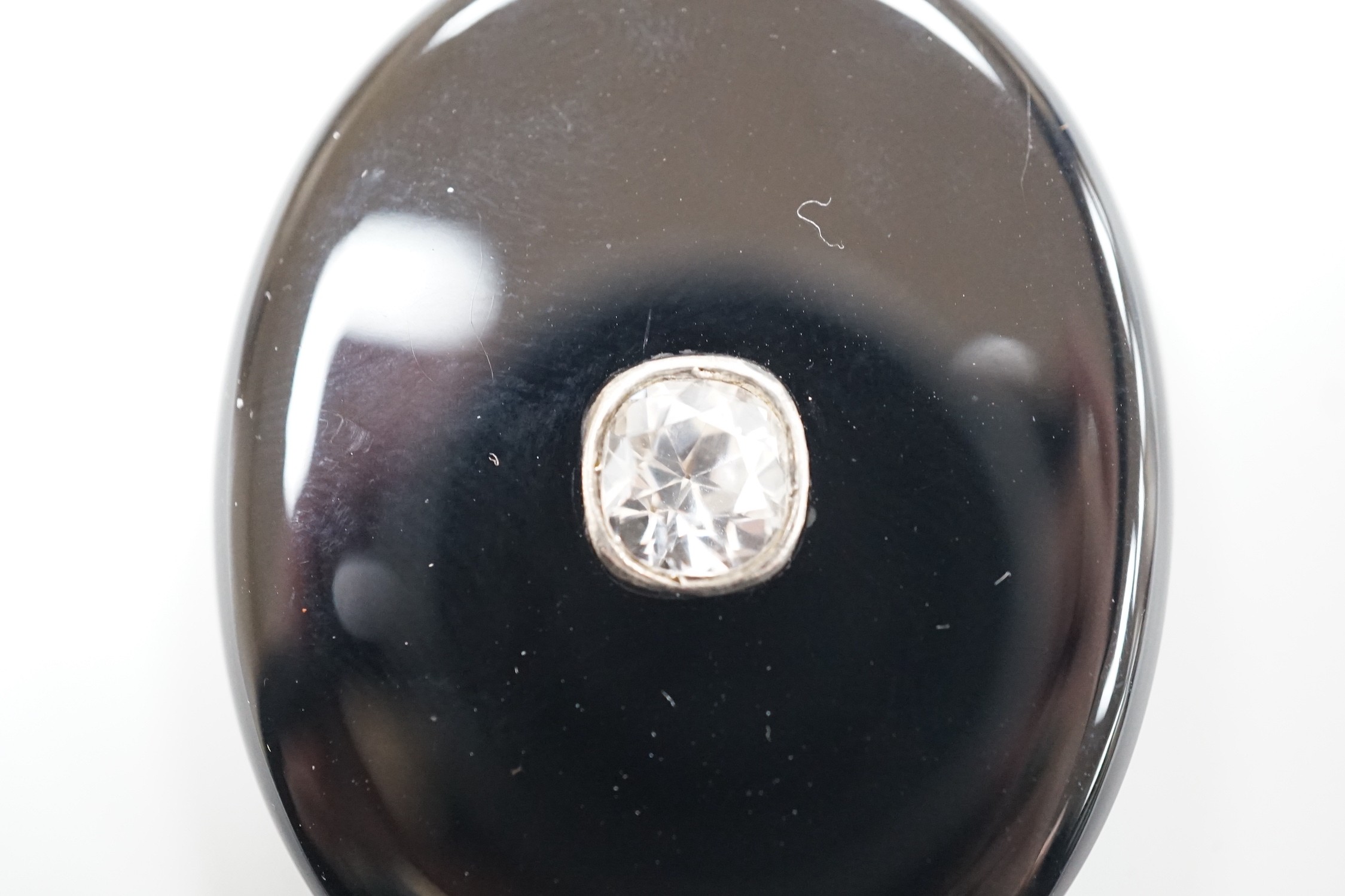 A Victorian yellow metal mounted black onyx oval locket, with black enamelled bale and set with an old cut white sapphire, overall 62mm